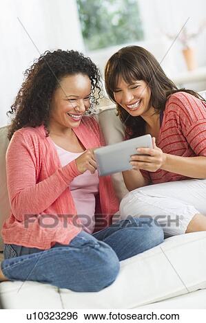 Stock Photograph - Two women sitting on sofa using digital tablets. Fotosearch