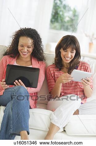Two women sitting on sofa using digital tablets View Large Photo Image Stock Photograph - Two women sitting on sofa using digital tablets. Fotosearch