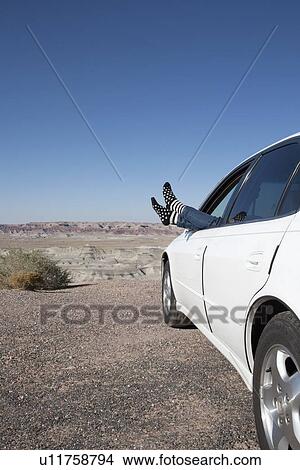 Picture - USA, Arizona, Winslow, Woman sticking feet out of car window parked in desert. Fotosearch