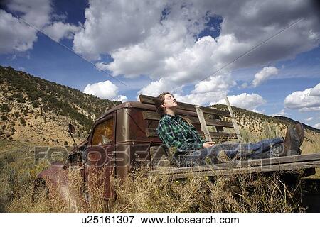 Stock Photo - USA, Colorado, Woman resting on bed of abandoned truck in desert. Fotosearch