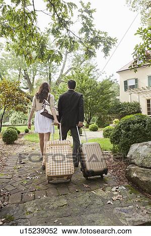 Stock Image - USA, New Jersey, Couple walking up path with luggage. Fotosearch