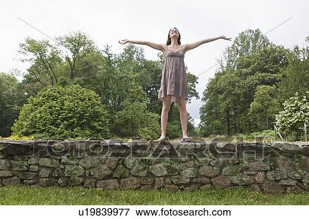 Stock Photo - USA, New Jersey, Happy woman standing on stone wall on field. Fotosearch