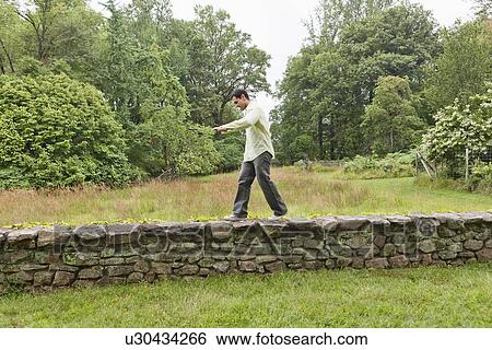 Stock Photograph - USA, New Jersey, Man walking on stone wall on field. Fotosearch