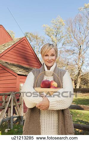 USA, New Jersey, Portrait of smiling woman holding basket with apples in front of cottage house in Autumn View Large Photo Image Stock Photography - USA, New Jersey, Portrait of smiling woman holding basket with apples in front of cottage house in Autumn. Fotosearch