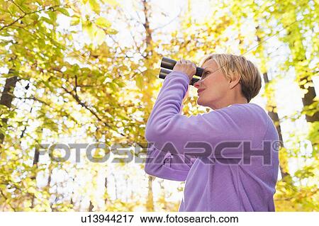 Stock Photo - USA, New Jersey, Woman looking through binoculars in Autumn forest. Fotosearch