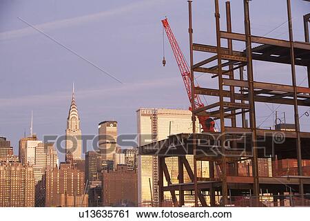 Stock Image - USA, New York City, Crane with unfinished structure and Manhattan skyline in background. Fotosearch