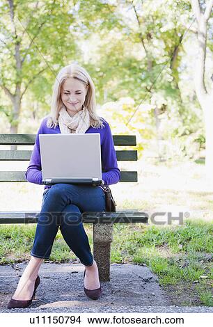 USA, New York, New York City, Manhattan, Central Park, Young woman sitting on bench and using laptop View Large Photo Image Picture - USA, New York, New York City, Manhattan, Central Park, Young woman sitting on bench and using laptop. Fotosearch