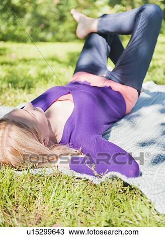 Stock Image - USA, New York, New York City, Manhattan, Central Park, Young woman lying on grass. Fotosearch