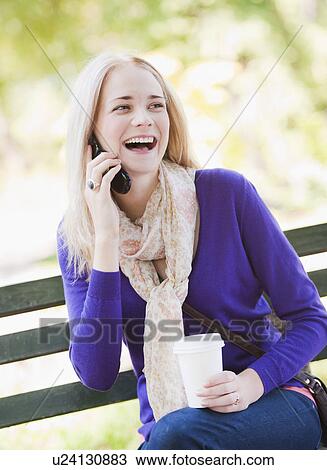USA, New York, New York City, Manhattan, Central Park, Young woman sitting on bench and talking on mobile phone View Large Photo Image Stock Image - USA, New York, New York City, Manhattan, Central Park, Young woman sitting on bench and talking on mobile phone. Fotosearch