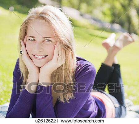 Stock Image - USA, New York, New York City, Manhattan, Central Park, Young woman lying on grass. Fotosearch