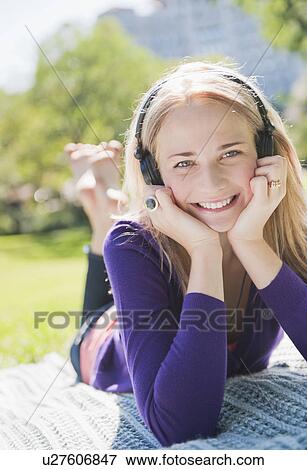 Stock Photo - USA, New York, New York City, Manhattan, Central Park, Young woman lying on grass and listening to music. Fotosearch