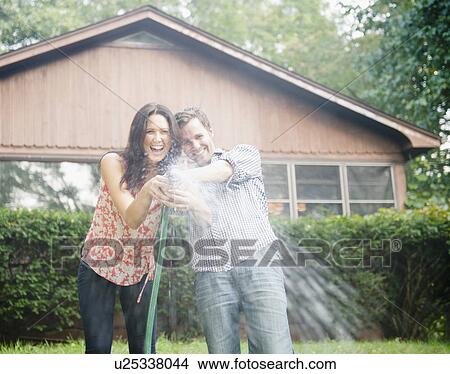 Picture - USA, New York, Putnam Valley, Roaring Brook Lake, Couple playing with hose. Fotosearch