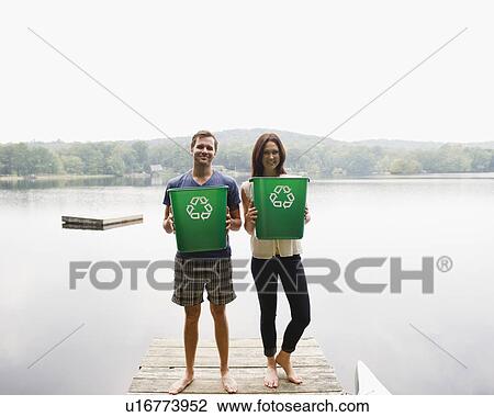 Stock Image - USA, New York, Putnam Valley, Roaring Brook Lake, Couple standing on pier with recycling bins. Fotosearch