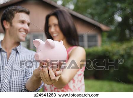 Stock Image - USA, New York, Putnam Valley, Roaring Brook Lake, Couple holding piggy bank. Fotosearch