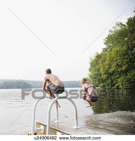 Stock Image - USA, New York, Putnam Valley, Roaring Brook Lake, Couple jumping from pier to lake. Fotosearch