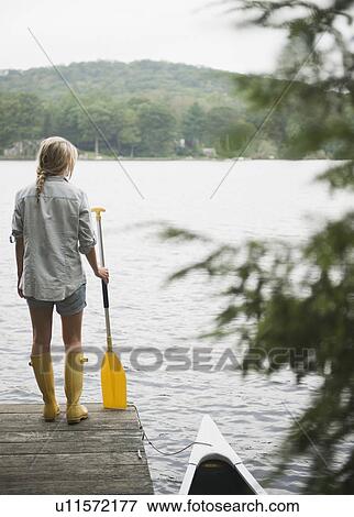 Stock Photo - USA, New York, Putnam Valley, Roaring Brook Lake, Woman standing on pier with paddle. Fotosearch