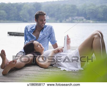 Stock Photo - USA, New York, Putnam Valley, Roaring Brook Lake, Couple relaxing on pier by lake. Fotosearch