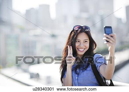 Stock Image - USA, Washington, Seattle, Woman photographing herself with smart phone outdoors. Fotosearch