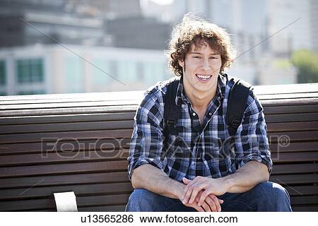 Stock Photograph - USA, Washington, Seattle, Young man sitting on bench. Fotosearch