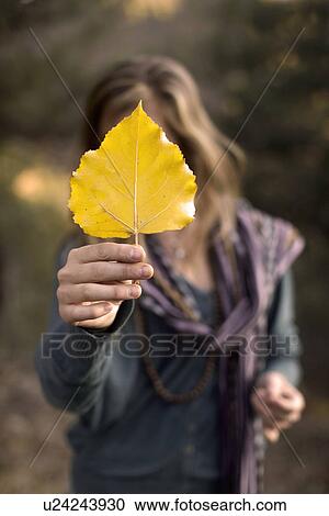 Stock Image - Woman holding leaf in front of face. Fotosearch