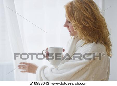 Stock Image - Woman in bathrobe looking out window. Fotosearch