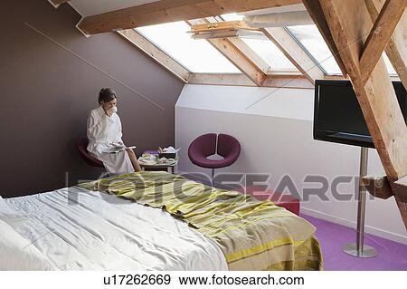 Stock Photo - Woman in bathrobe sitting in bedroom. Fotosearch