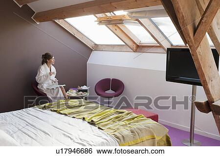 Stock Photograph - Woman in bathrobe sitting in bedroom. Fotosearch