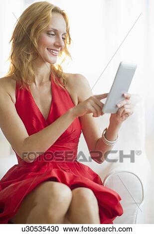 Stock Image - Woman in red dress using tablet pc, studio shot. Fotosearch