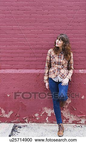 Stock Image - Woman leaning against purple brick wall. Fotosearch