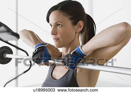 Stock Image - Woman lifting barbell in gym. Fotosearch