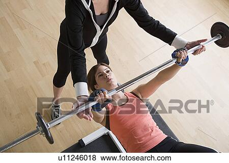 Woman lifting barbell while instructor assisting her View Large Photo Image Stock Photo - Woman lifting barbell while instructor assisting her. Fotosearch
