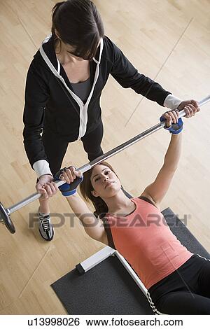 Woman lifting barbell while instructor assisting her View Large Photo Image Stock Photograph - Woman lifting barbell while instructor assisting her. Fotosearch