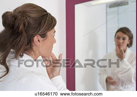 Stock Image - Woman looking in bathroom mirror. Fotosearch