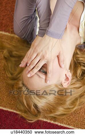 Stock Image - Woman lying on floor covering eyes. Fotosearch