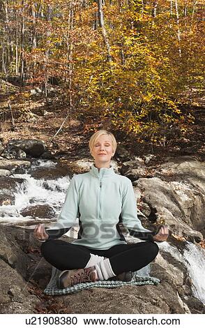Stock Image - Woman meditating by stream in forest. Fotosearch