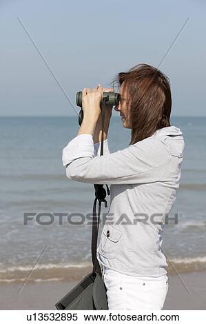 Stock Photography - Woman on beach looking through binoculars. Fotosearch