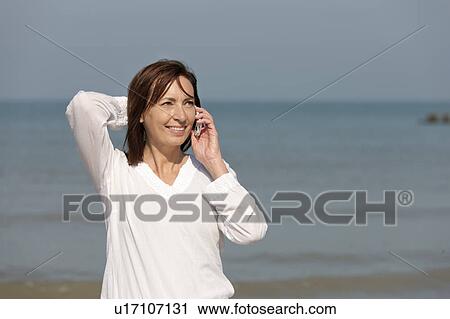 Stock Image - Woman on beach talking on phone. Fotosearch