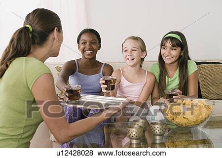 Stock Photo - Woman serving drinks for three girls (10-11) at slumber party. Fotosearch