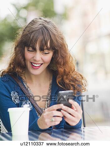 Stock Photo - Woman sitting in sidewalk cafe and texting on mobile phone. Fotosearch