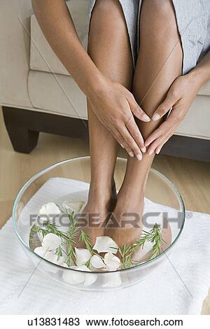 Stock Image - Woman soaking feet in water with petals. Fotosearch