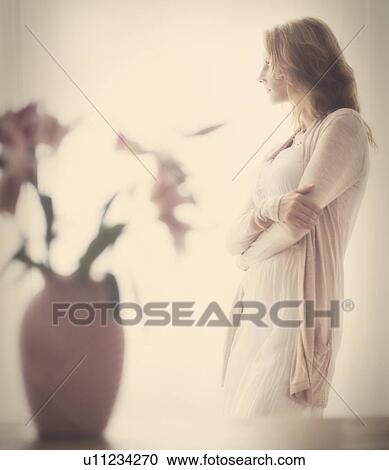 Stock Image - Woman standing behind vase, studio shot. Fotosearch