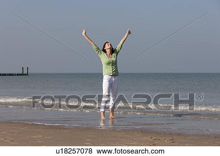 Stock Photo - Woman standing on beach with arms raised. Fotosearch