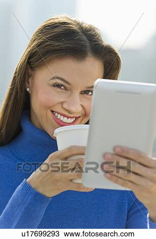 Stock Image - Woman working on digital tablet and drinking coffee. Fotosearch