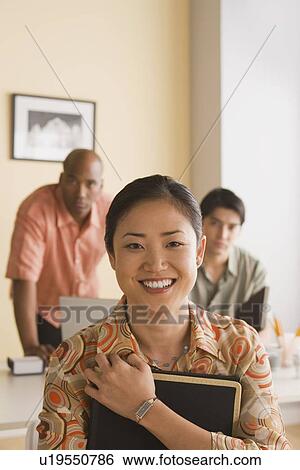 Young businesswoman posing for portrait with two colleagues in background View Large Photo Image Stock Photograph - Young businesswoman posing for portrait with two colleagues in background. Fotosearch