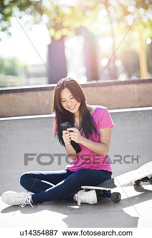 Young chinese woman text messaging while sitting on skateboard View Large Photo Image Stock Photo - Young chinese woman text messaging while sitting on skateboard. Fotosearch