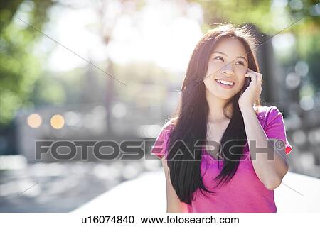 Stock Image - Young chinese woman using mobile phone outdoors. Fotosearch