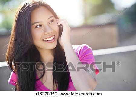 Stock Image - Young chinese woman using mobile phone outdoors. Fotosearch