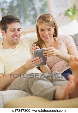 Young couple sitting on sofa with digital tablet View Large Photo Image Stock Image - Young couple sitting on sofa with digital tablet. Fotosearch