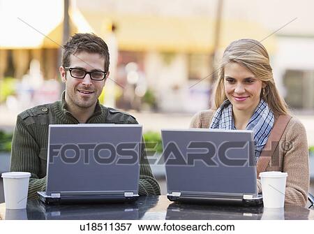 Young couple sitting with laptops in sidewalk cafe View Large Photo Image Stock Photo - Young couple sitting with laptops in sidewalk cafe. Fotosearch