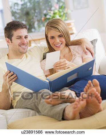Stock Photograph - Young couple watching photos on sofa. Fotosearch
